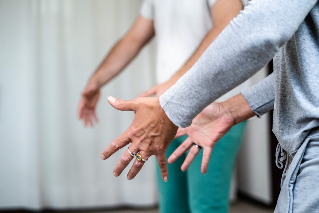 Zwei Peronen bei Qi Gong-Übung: im Stehen, Hände vorm Körper, die Hände zeigen zueinander als würden sie etwas halten.